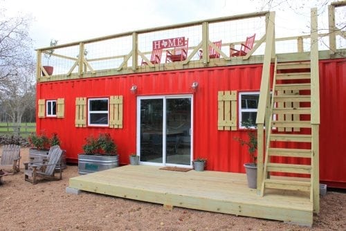red cool shipping container home with wooden porch built on top. 