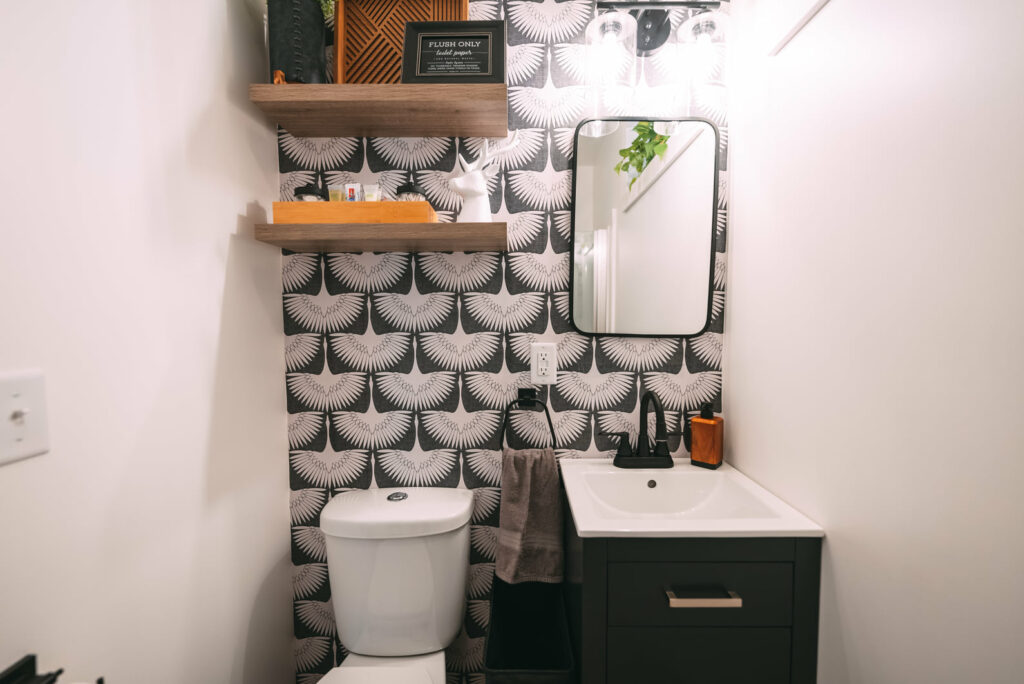 Toilet, bathroom sink and mirror against black and white design wall paper
