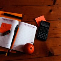 black scientific calculator, orange, and notebook on table