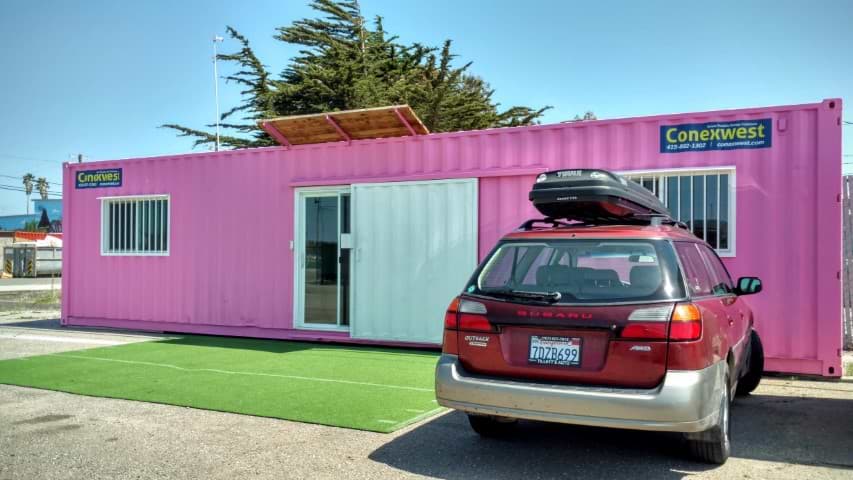 a car parked outside of a pink colored container home